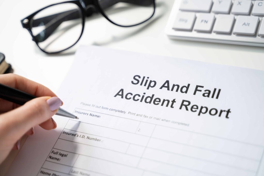 Hand filling out slip and fall accident report form on desk, personal injury claim and insurance documentation concept