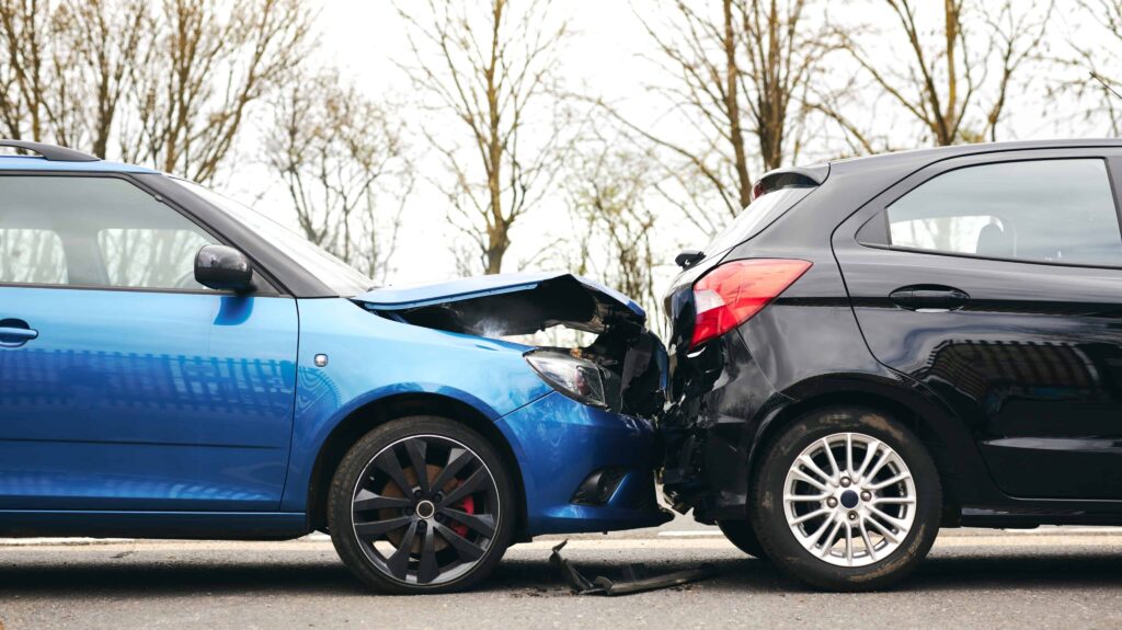 Rear-end car accident showing a blue car crashed into a black car, with visible front-end damage on a city road