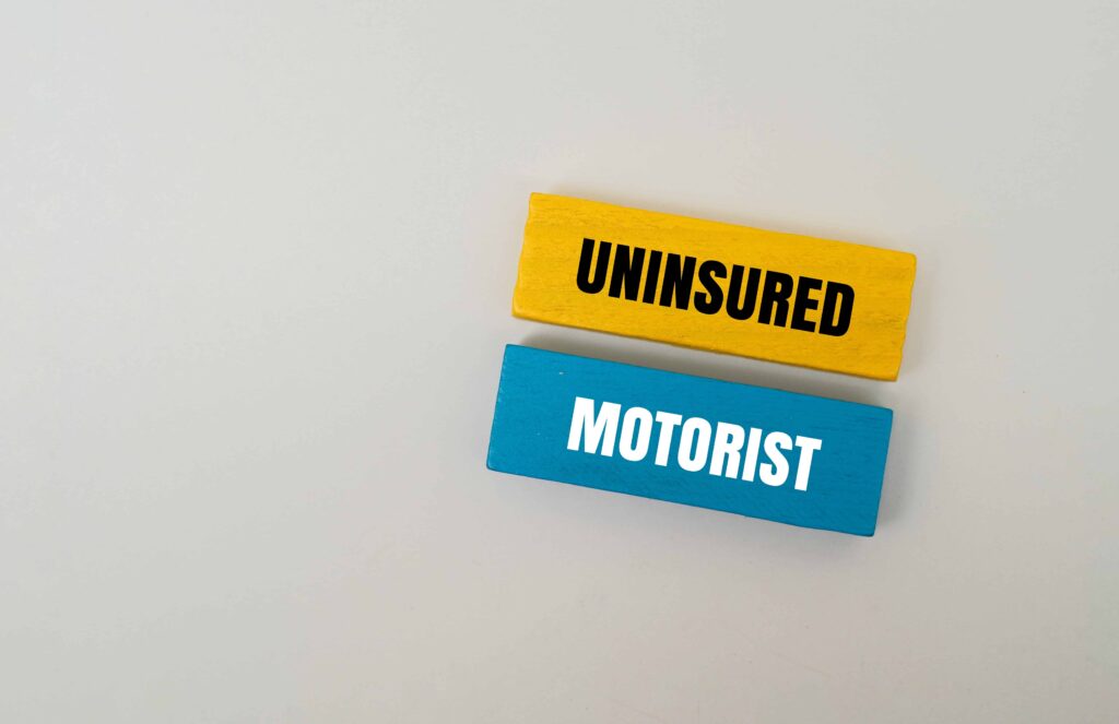 Uninsured motorist concept with yellow and blue blocks labeled &lsquo;Uninsured&rsquo; and &lsquo;Motorist&rsquo; on a white background, representing auto insurance coverage gaps