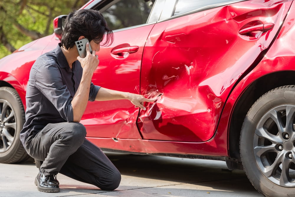 Man on the phone inspecting damage to his car after a crash
